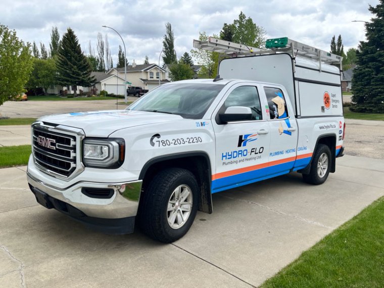 A white service truck featuring a blue and orange logo, parked in Alberta, Canada