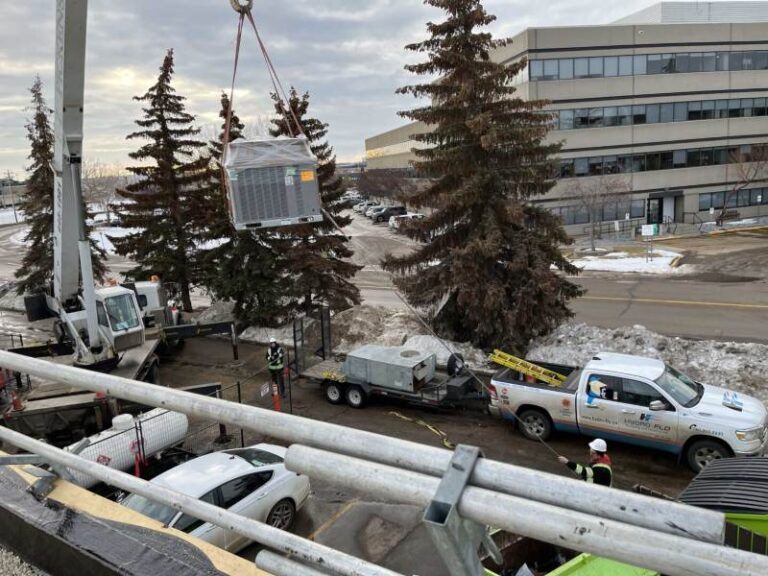 A crane elevates an Air conditioner, representing commercial HVAC installation in Edmonton, AB.